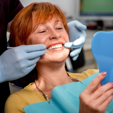 Woman in dental chair looking at her smile in mirror