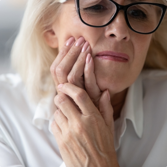 Woman with glasses holding her jaw in pain