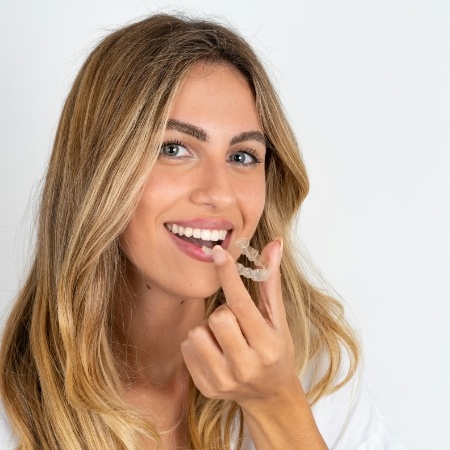 Smiling woman holding Invisalign clear aligner in Falls Church