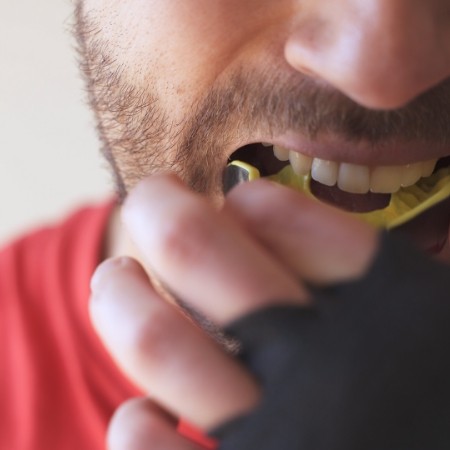 Close up of man placing yellow mouthguard over his teeth