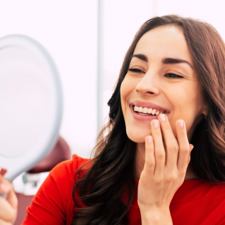 Young woman in dental chair admiring her smile in mirror