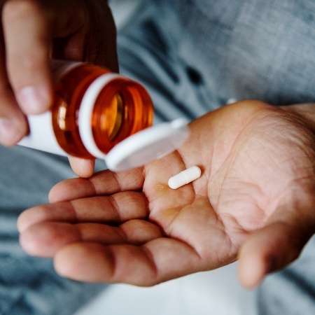 Person pouring a pill into their hand from an orange bottle